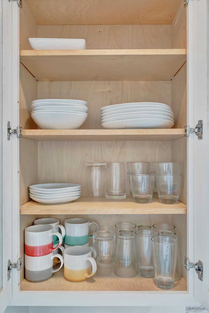 Your kitchen is fully stocked with everything you need—crisp white dishes, colorful mugs, and plenty of glassware ready for morning coffee or evening cocktails.