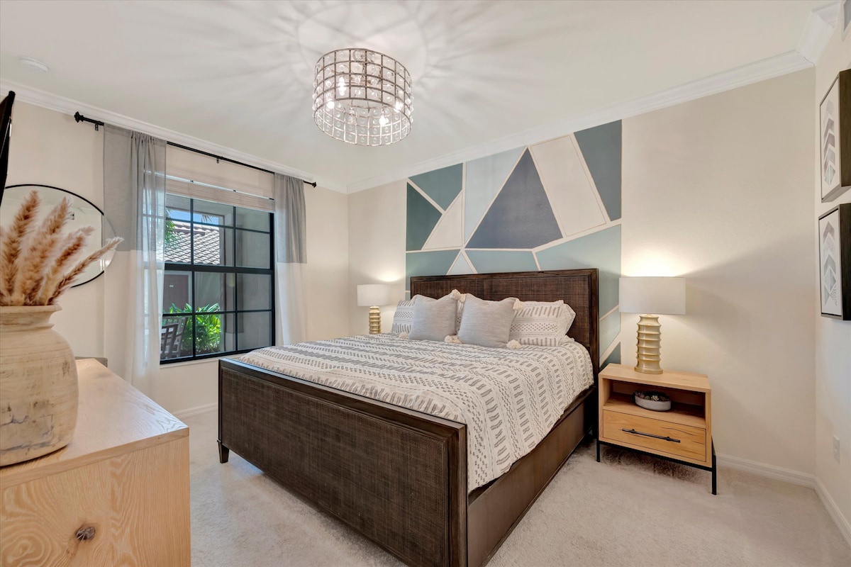 Your peaceful retreat features a plush queen bed beneath a geometric accent wall, bathed in natural light from the oversized window. Soft textiles and warm wood tones create the perfect setting for restful nights.