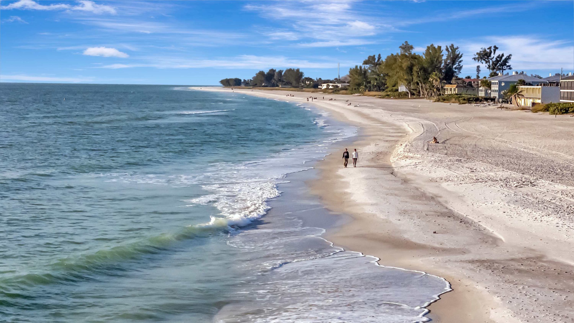 A pristine stretch of sandy coastline curves along calm turquoise waters, with beachside properties and swaying palms creating an inviting backdrop for your coastal getaway.
