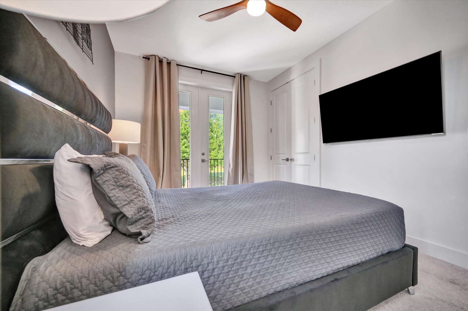 Sink into plush gray bedding under a gently spinning ceiling fan. Natural light spills through French doors, while your wall-mounted TV awaits cozy movie nights.