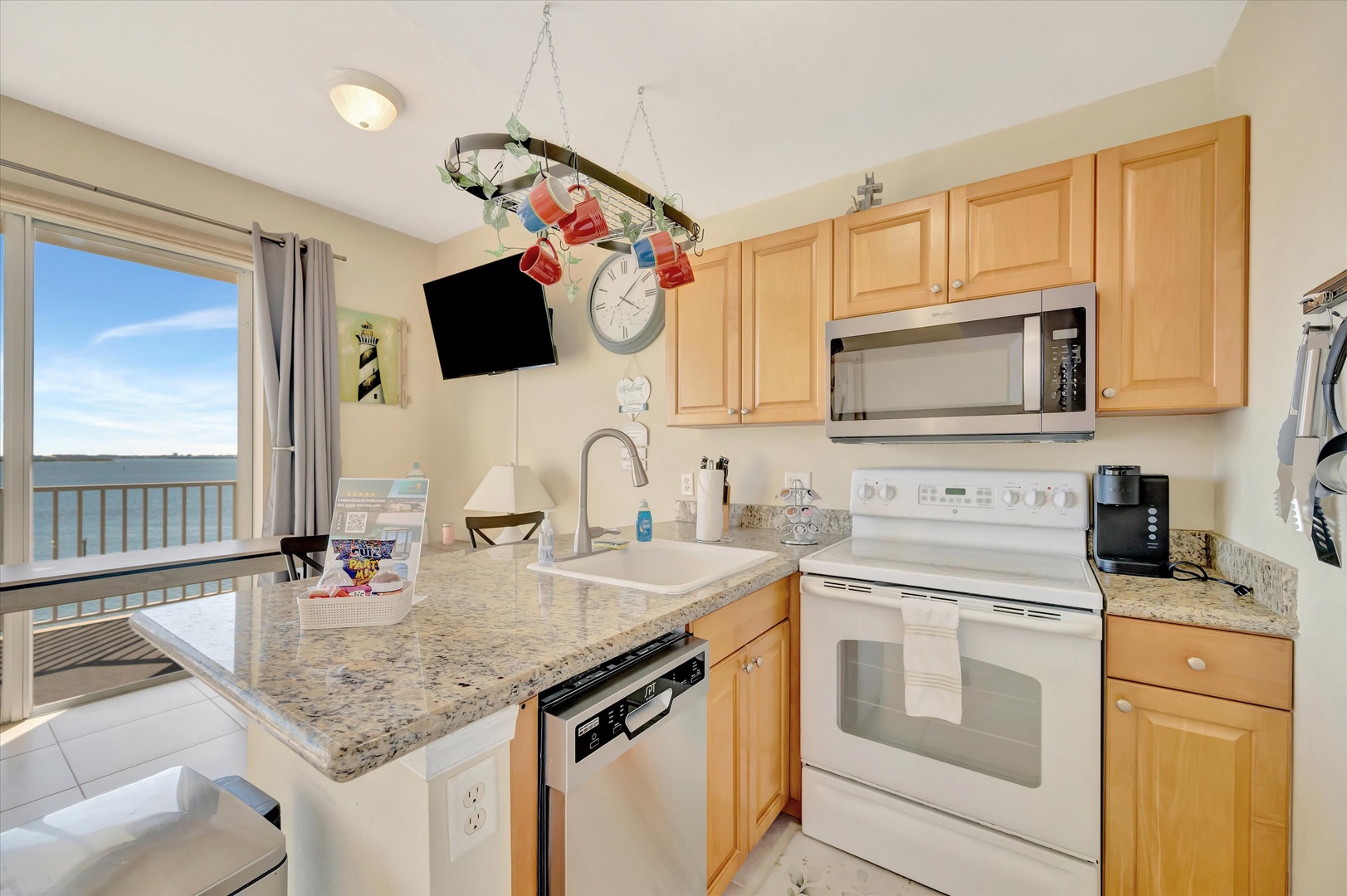 Your fully equipped kitchen opens to stunning ocean views through the balcony doors, with modern appliances and a breakfast bar ready for morning coffee as you watch the waves.
