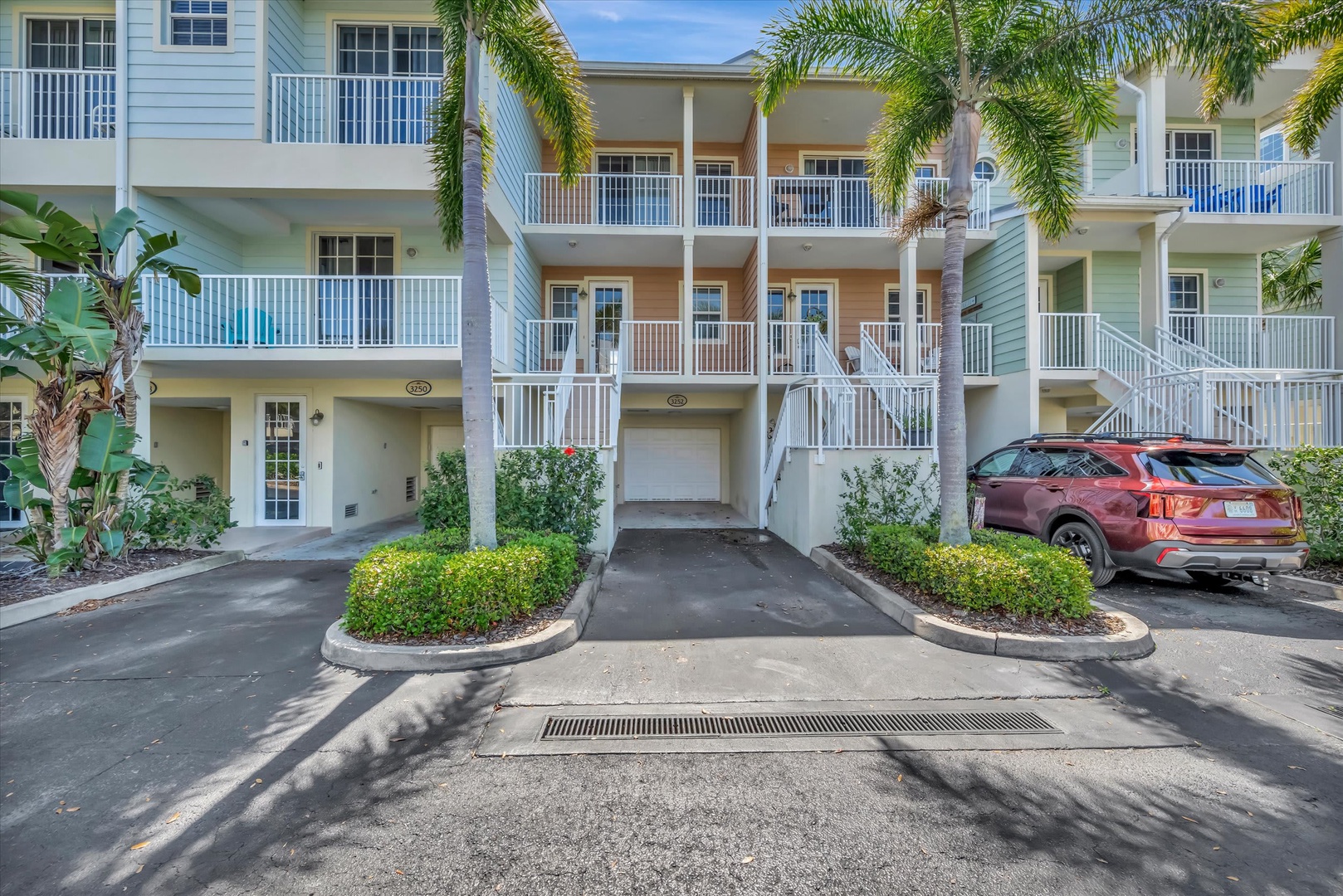 Multi-story vacation property with private balconies and tropical landscaping featuring palm trees and lush greenery, offering convenient covered parking for guests.