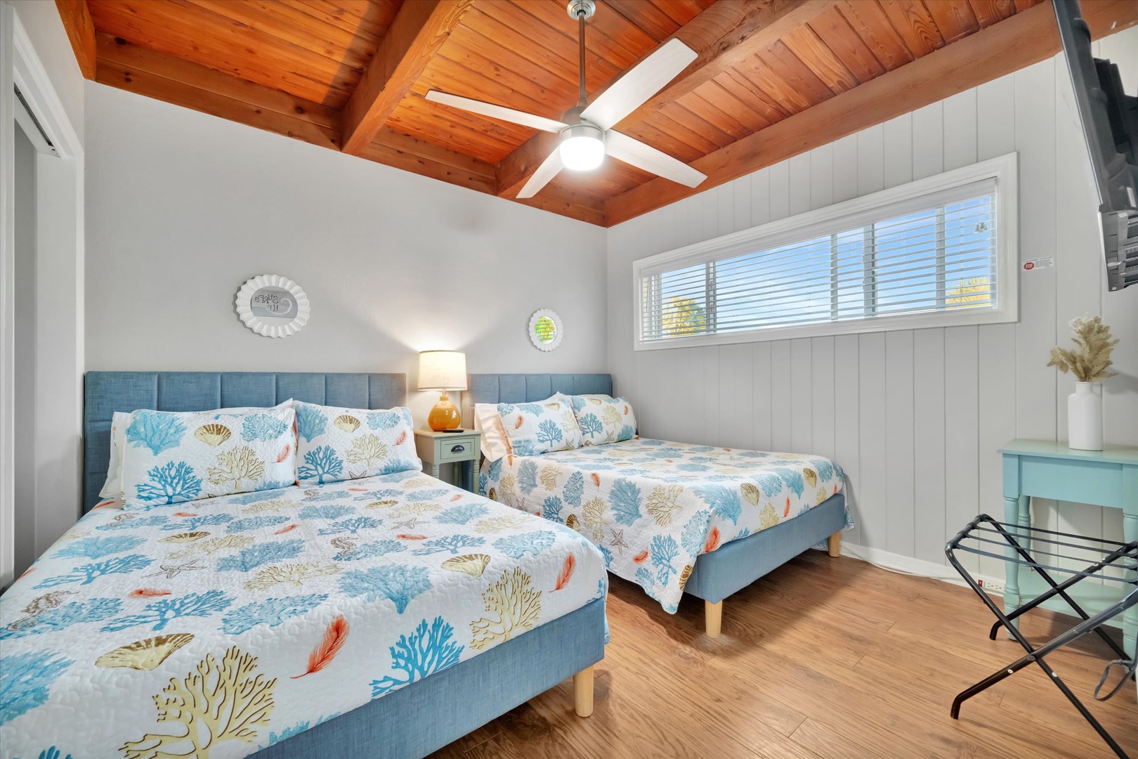 Unwind in your coastal-inspired bedroom with vaulted wood ceilings and two plush beds dressed in cheerful coral prints. Natural light pours in, highlighting the warm wood floors and inviting you to settle in for a restful stay.