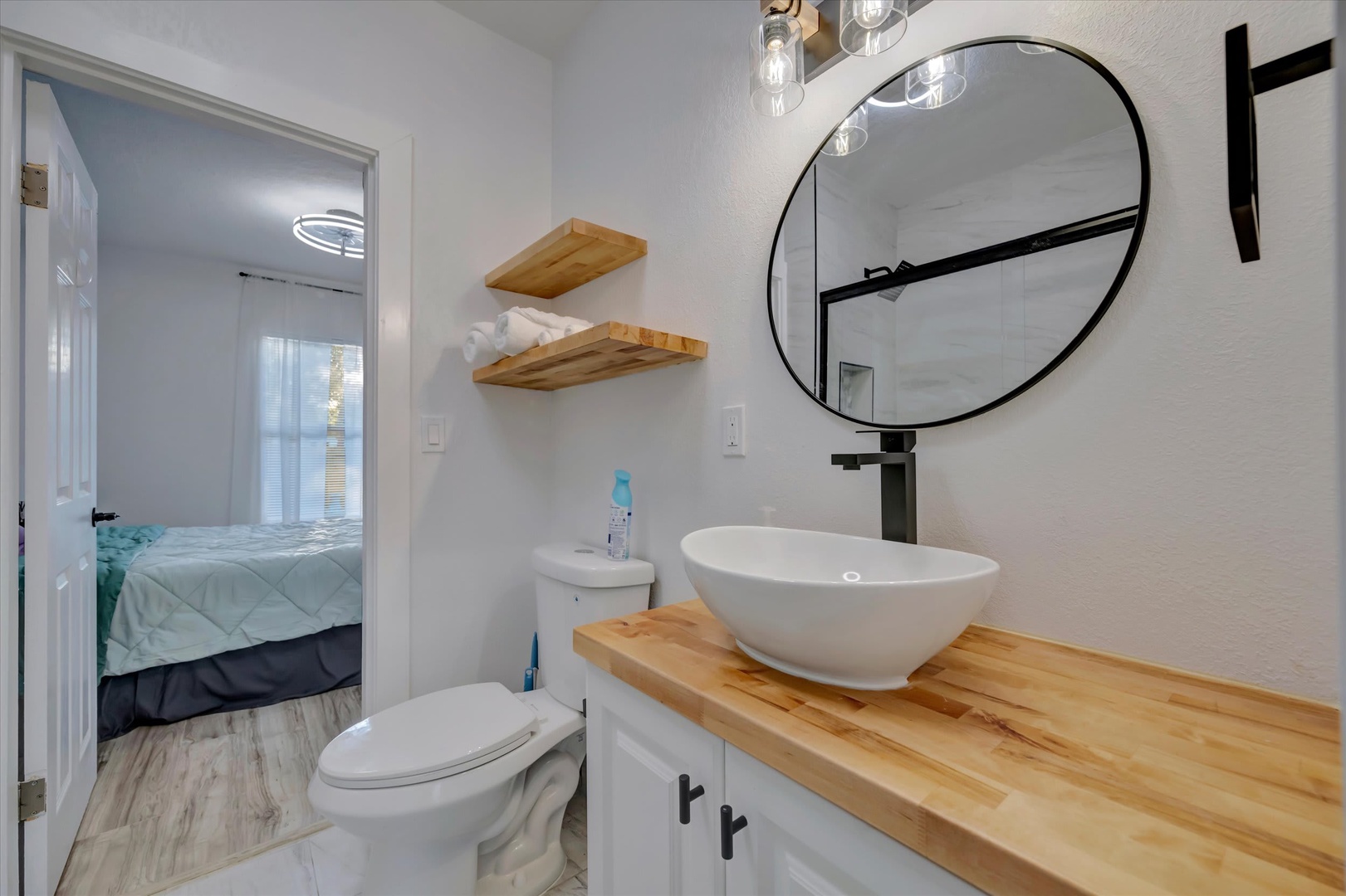 Freshen up in your stylish bathroom featuring a modern vessel sink, warm wood accents, and a bold round mirror. Soft towels and thoughtful shelving make your stay comfortable and convenient.