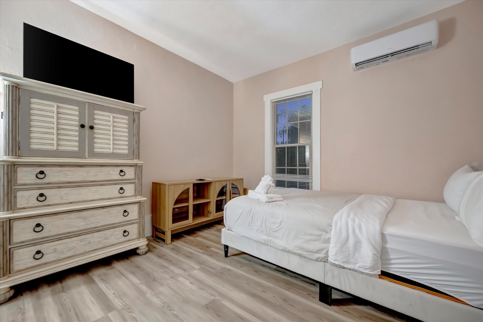 Step into your peaceful retreat where cool comfort meets coastal charm. Soft pink walls and light wood floors create a serene sanctuary, while the dresser and bedside storage keep everything perfectly organized for your stay.