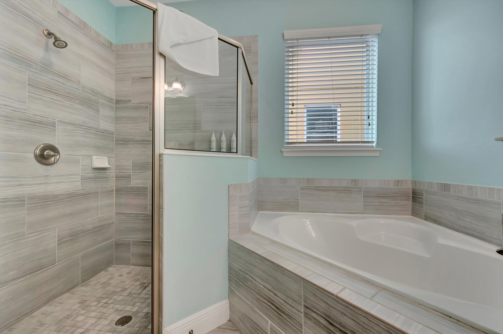Your private bathroom features calming aqua walls, elegant tile work, and a spacious walk-in shower alongside a relaxing soaking tub—perfect for unwinding after exploring the area.