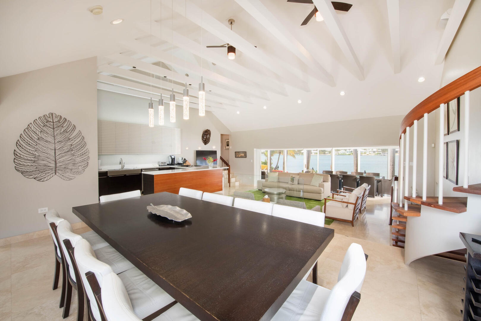 The main villa's great room features vaulted ceilings, an open concept design with multi-levels, and waterfront views throughout. The formal dining table seats 10 guests.