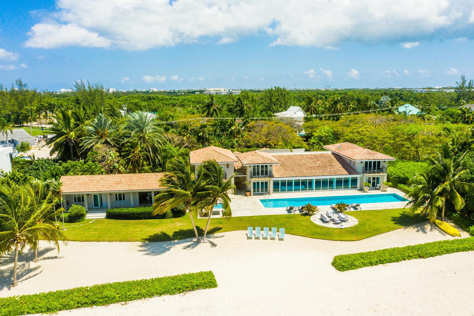 Aerial view of the main house, pool deck, beachfront, and detached guest cottage with outdoor kitchen.