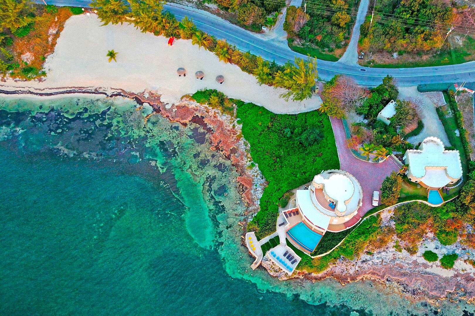 Aerial view of the estate's private beach. 3 palapas are set up on the beach for shade.