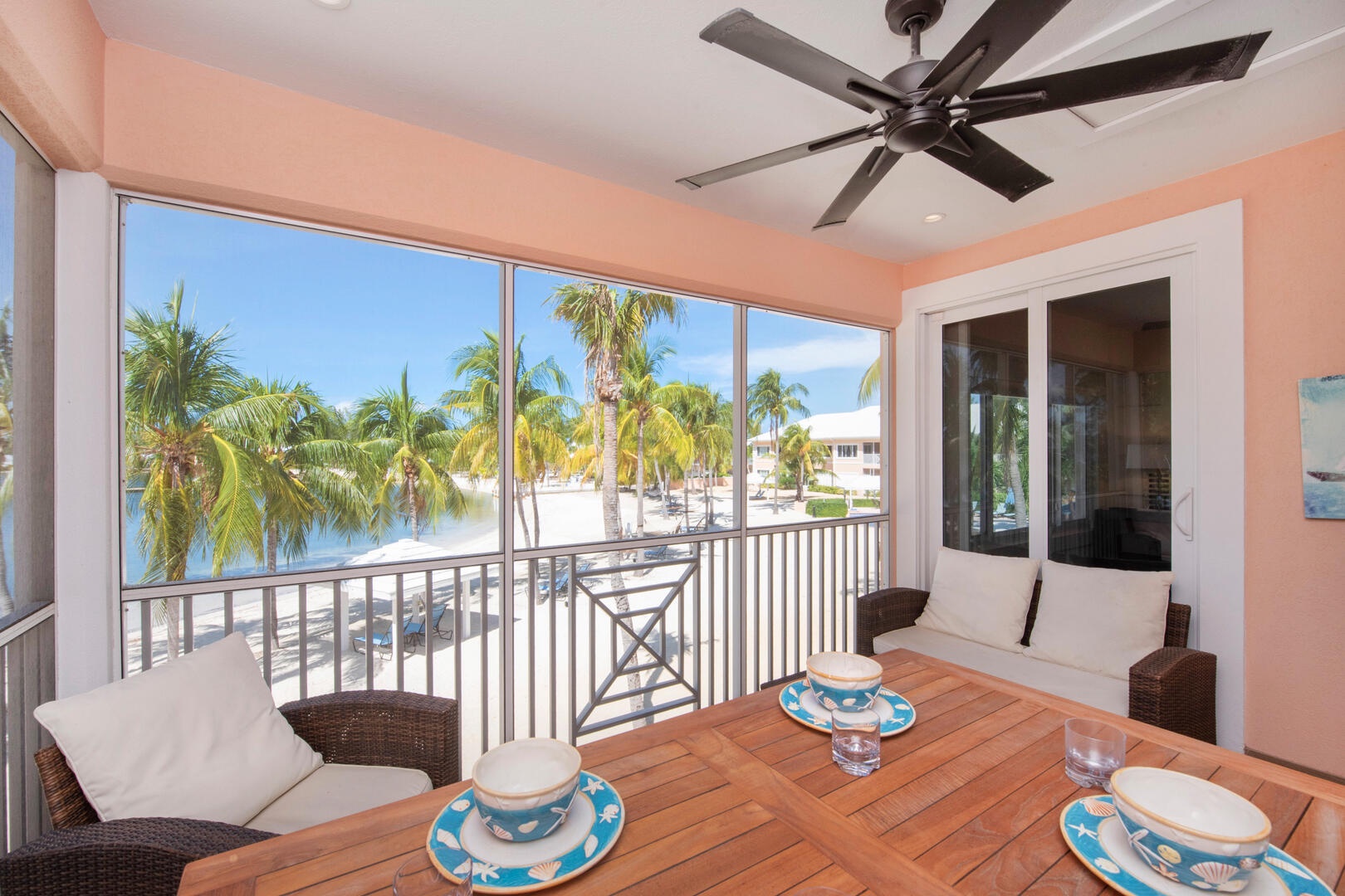 The private screened balcony overlooks the backyard beachfront and comes furnished with a dining table and patio seating.