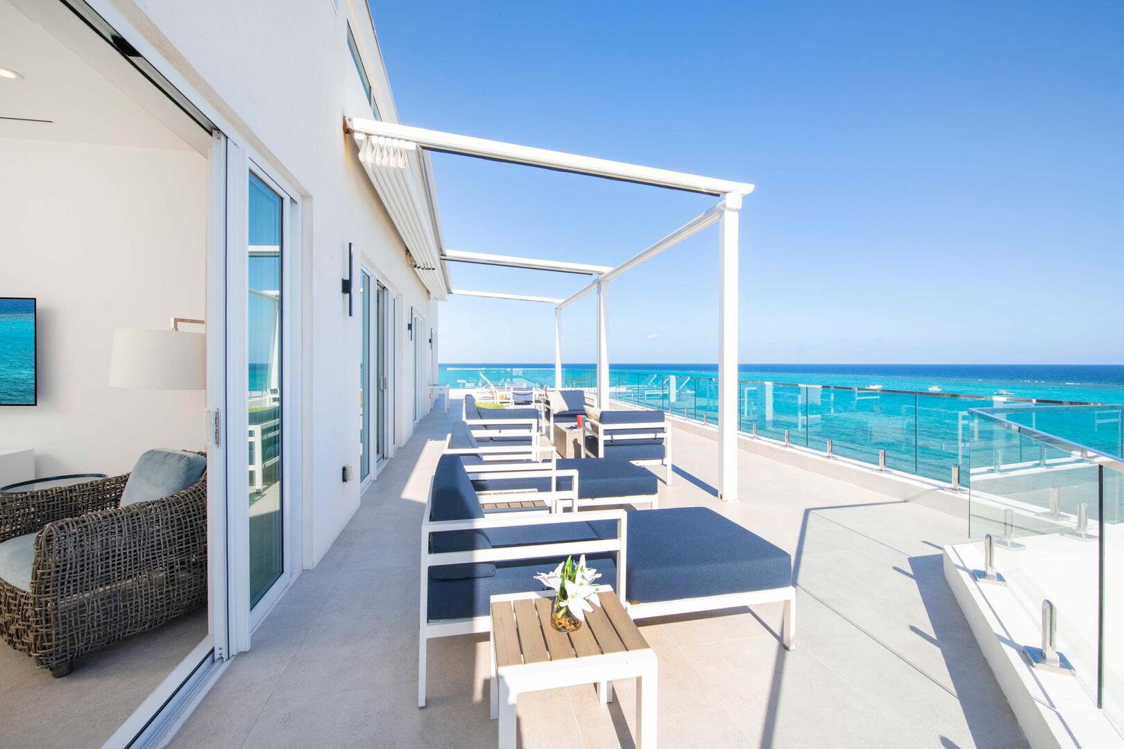 Walk-out access from the living room onto the oversized ocean balcony furnished with sun beds and an alfresco dining table.