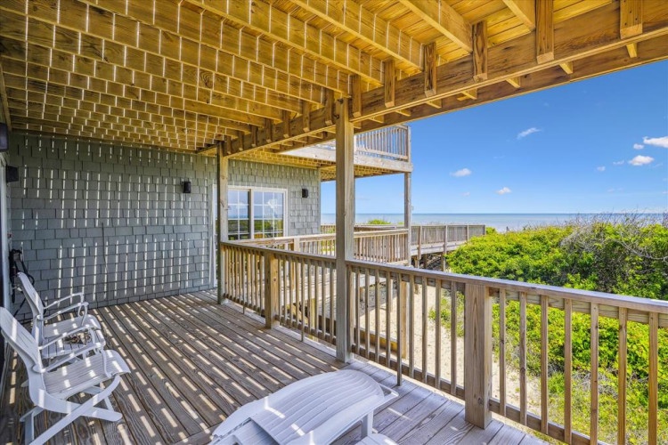 A covered beachfront deck where you can relax with ocean breezes and watch waves roll in while lush coastal greenery frames your view of endless blue horizons.