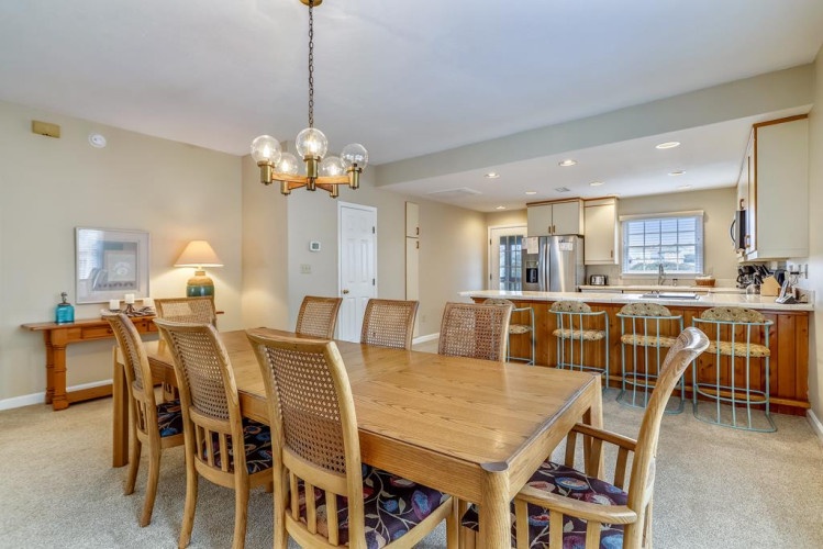 Step into an inviting open-plan space where gathering feels effortless. Your dining table seats everyone comfortably, with warm wood tones and a stylish chandelier overhead, while the modern kitchen awaits your culinary adventures.