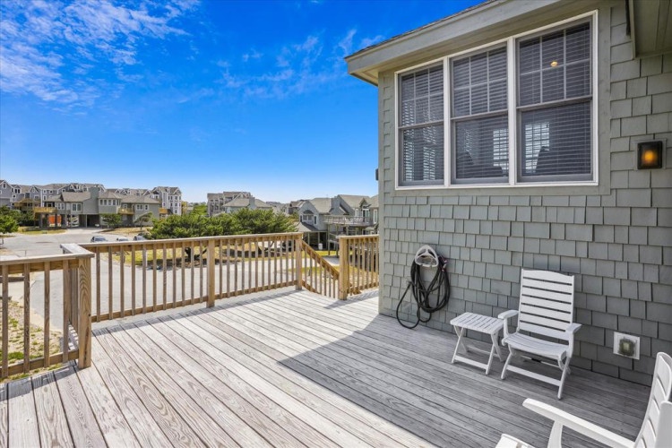 A spacious deck overlooks the surrounding coastal neighborhood, framed by clear blue skies and neighboring rooftops—a perfect backdrop for your beachside getaway.