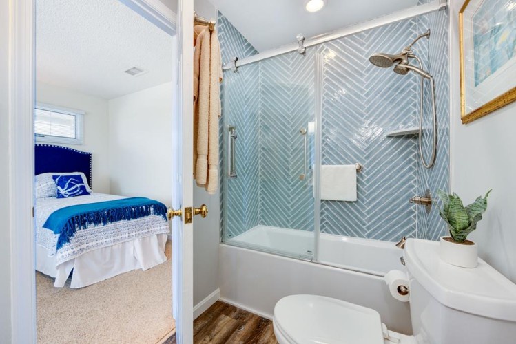 Your private bathroom features a stylish chevron-tiled tub-shower combo and modern glass door, combining function with refreshing coastal-inspired design.