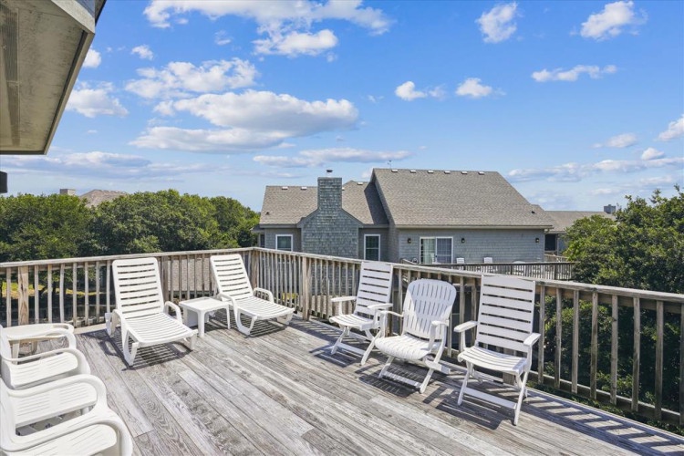 Elevated deck features lounge chairs overlooking neighboring properties and lush greenery, providing an outdoor relaxation space under open skies.