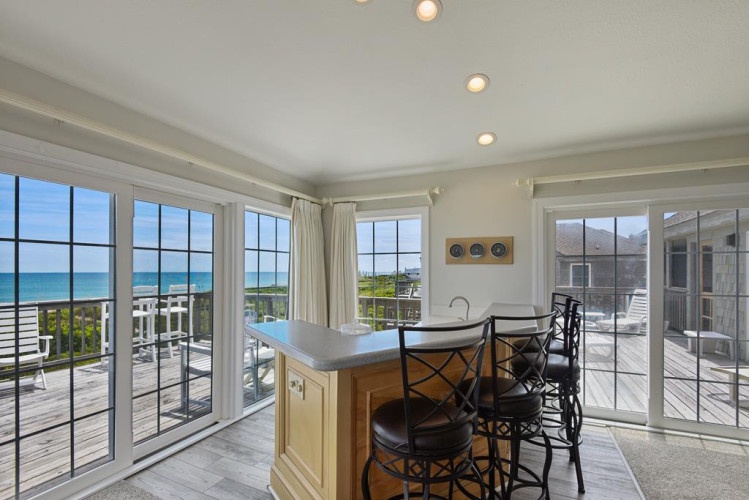 Enjoy your morning coffee at this bright kitchen island while soaking in stunning ocean views through floor-to-ceiling windows that frame the endless blue horizon.
