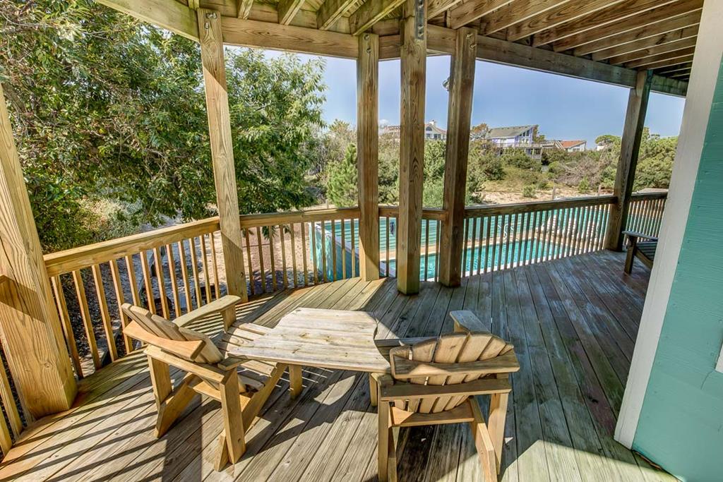 The spacious covered deck showcases turquoise pool waters and coastal dunes beyond, offering a peaceful waterside retreat for outdoor dining and relaxation throughout your stay.