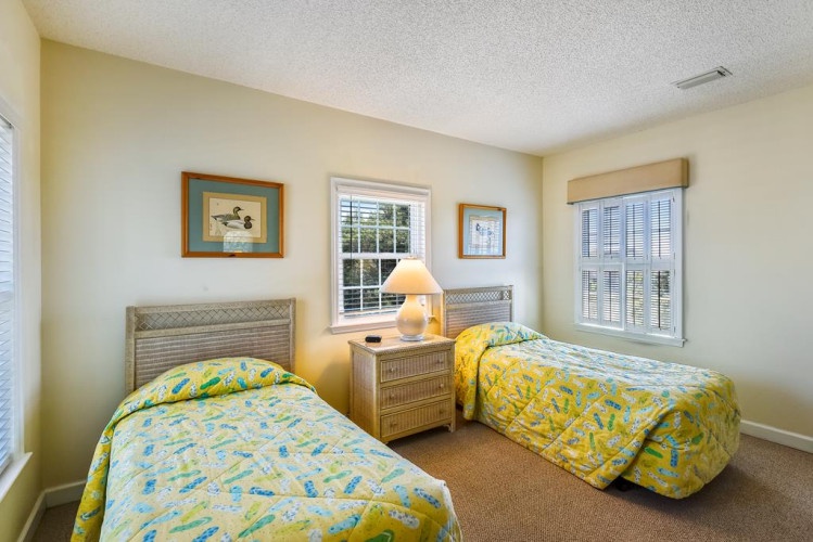 Your cheerful twin bedroom features sunny yellow linens and soft natural light streaming through plantation shutters, creating a bright and welcoming retreat for restful nights.
