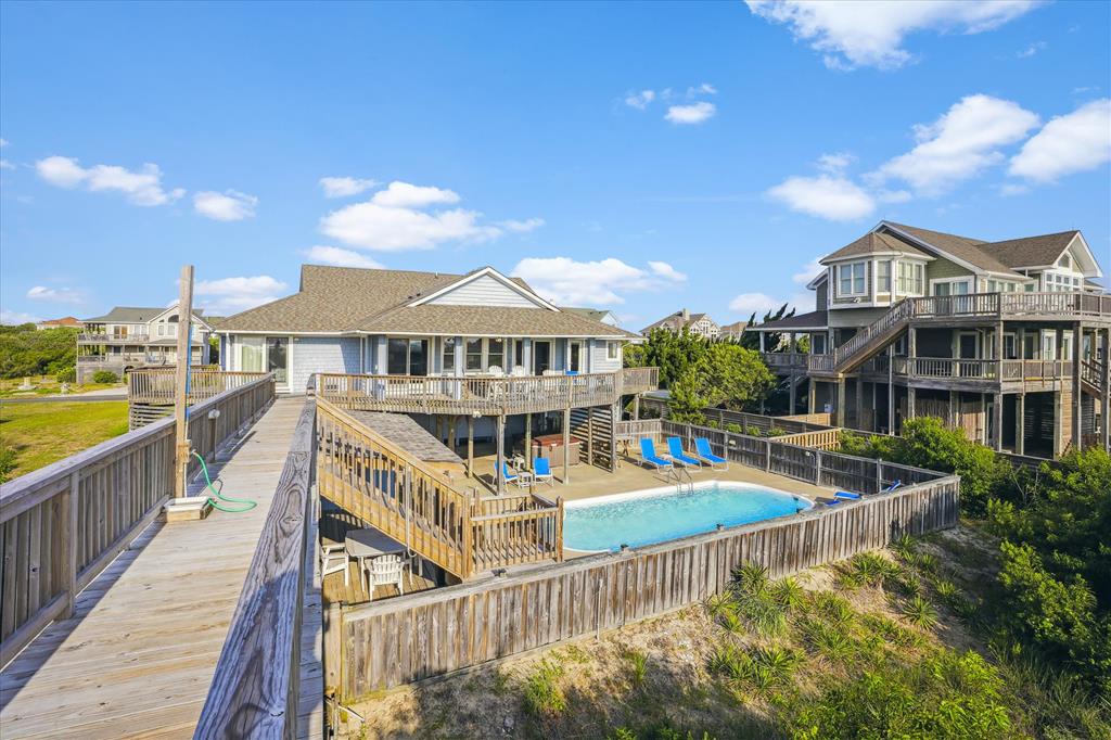 Coastal vacation homes with private pool and elevated boardwalks set against a bright blue sky in a peaceful beachside neighborhood.