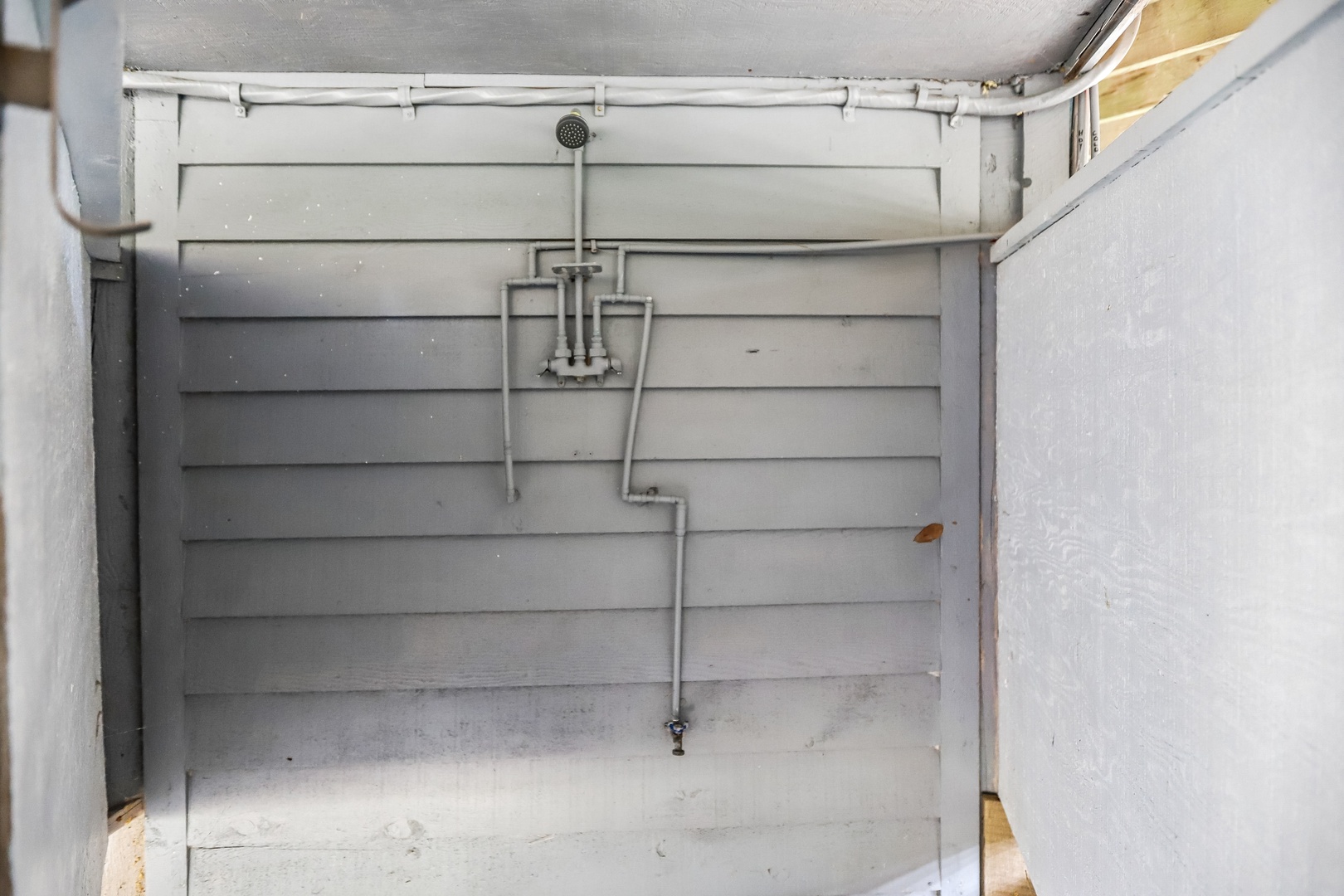 An outdoor shower for rinsing off after a day at the beach or pool, featuring a simple overhead rainfall design against a clean white backdrop.