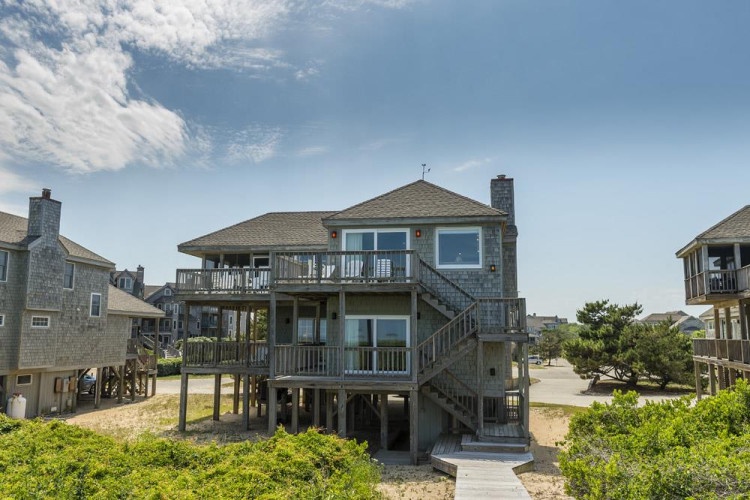 A charming coastal retreat with elevated decks and coastal-style architecture, situated in a peaceful beachside neighborhood with natural dune landscaping.