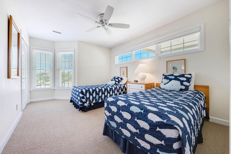 Your tranquil bedroom awaits with twin beds dressed in cheerful whale-patterned linens, crisp natural light from plantation shutters, and a gentle ceiling fan for peaceful coastal nights.