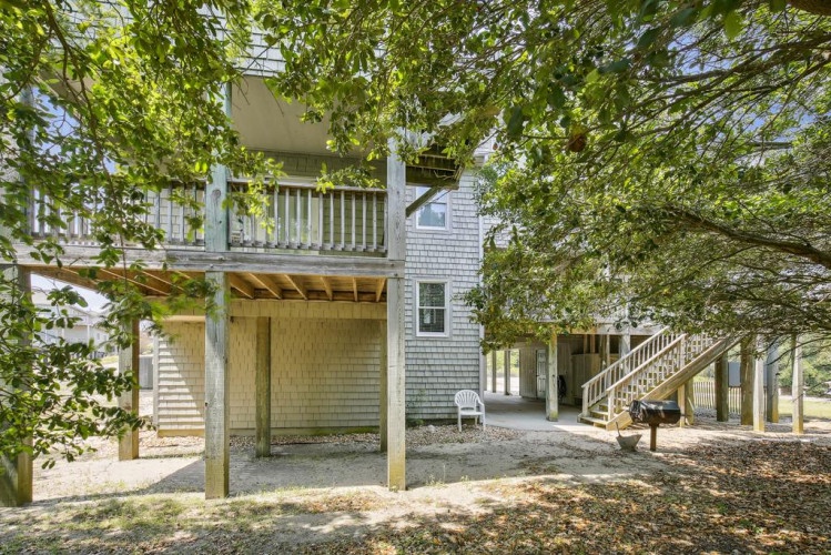 A charming coastal property nestled among mature trees, offering covered parking and outdoor living spaces with a classic shingled exterior and multiple balconies.