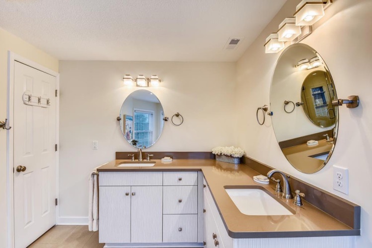 Your private bathroom features dual vanities with elegant oval mirrors, warm lighting, and plenty of counter space for your morning routine.