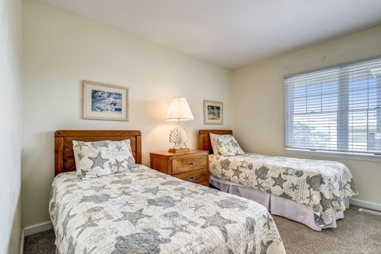 Two cozy twin beds with coastal-inspired bedding create a serene retreat. A shared nightstand and soft lamp light set the tone for peaceful mornings and restful nights.