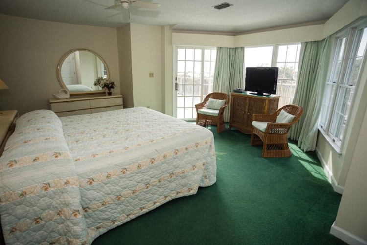 Relax in your bright, spacious bedroom featuring a comfortable bed, cozy seating area, and private balcony access with natural light streaming through large windows—perfect for unwinding after a day of adventure.