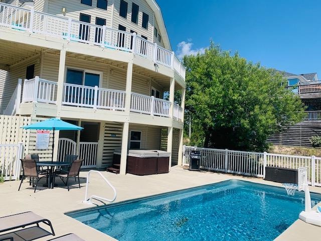 A spacious coastal retreat featuring a private pool, hot tub, outdoor dining area, and multiple balconies under clear blue skies—your perfect getaway for sun-soaked relaxation and memorable moments.