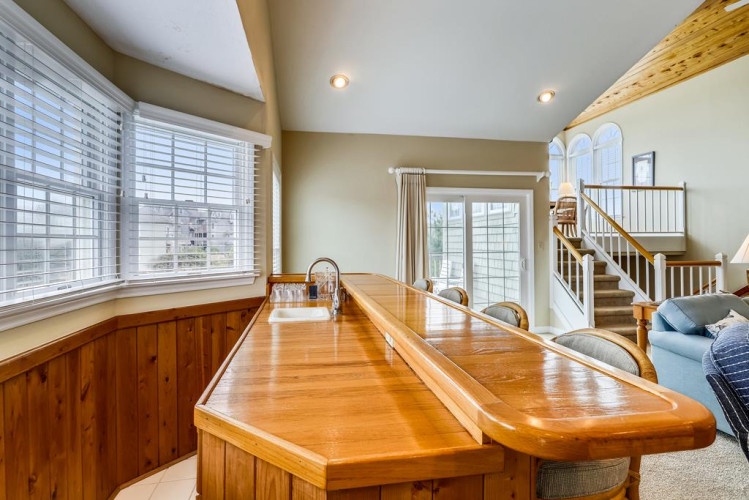 Gather around this spacious wooden bar with gleaming countertops, perfect for morning coffee or evening cocktails as natural light pours through the windows.