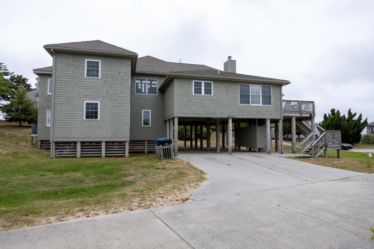 Spacious coastal home elevated on stilts with ample parking and deck access, nestled among coastal greenery and steps from sandy shores.
