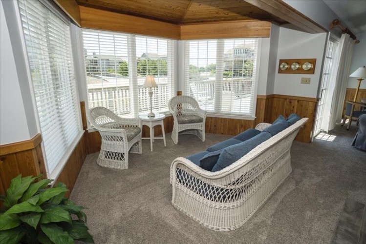 Unwind in this charming sunroom with wicker seating, vaulted wood ceilings, and bright windows framing serene outdoor views—your perfect spot to relax with morning coffee or a good book.