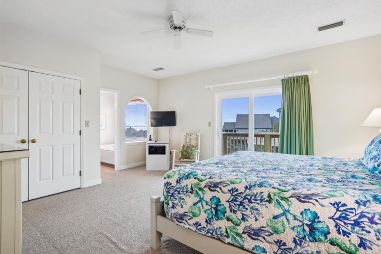 Wake up to serene water views framed by soft green curtains. Your bedroom offers a peaceful retreat with ceiling fan, TV, and a comforting space to unwind after exploring the coast.