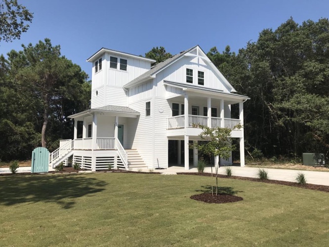 A striking coastal-style home situated in a peaceful wooded setting, featuring multiple balconies and a spacious lawn perfect for outdoor activities.