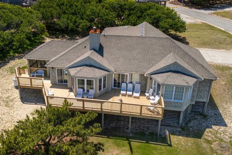 Coastal retreat featuring spacious wraparound decks, mature oak trees, and beachfront access, nestled in a quiet residential neighborhood.