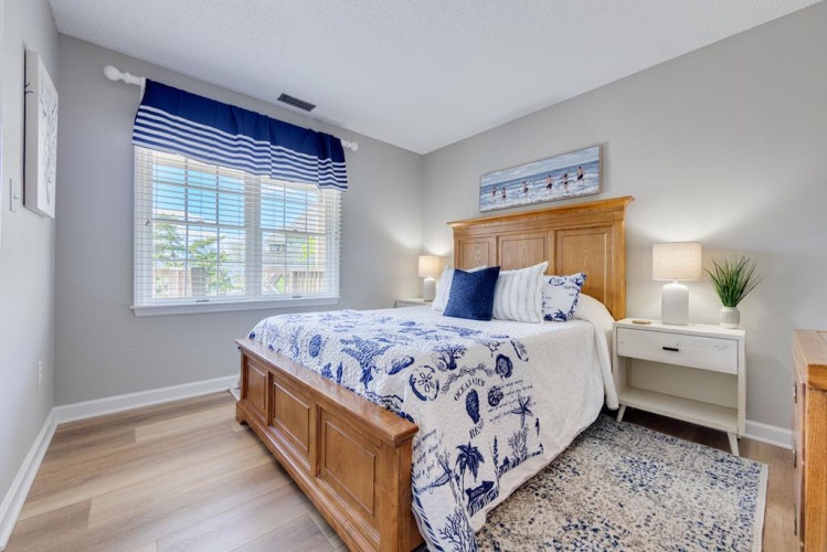 Drift off in your coastal-inspired bedroom, where soft gray walls and ocean-themed linens create a serene retreat. Natural light filters through crisp blinds, inviting restful mornings and peaceful nights.