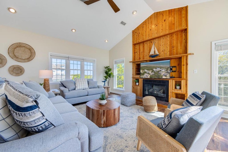 Sink into plush seating as vaulted ceilings and coastal charm invite you to relax by the warm fireplace, framed by a stunning wood accent wall.
