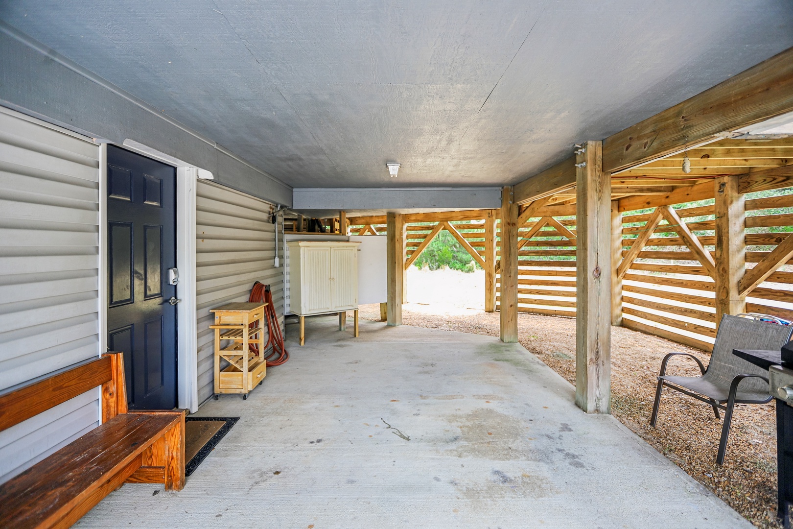 A covered carport with rustic timber framing provides sheltered parking and storage space at the property entrance.