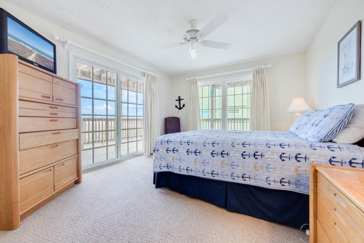Wake to ocean views through sliding glass doors and picture windows. Your coastal bedroom offers beach-themed comfort, ceiling fan breezes, and direct balcony access to the waterfront.