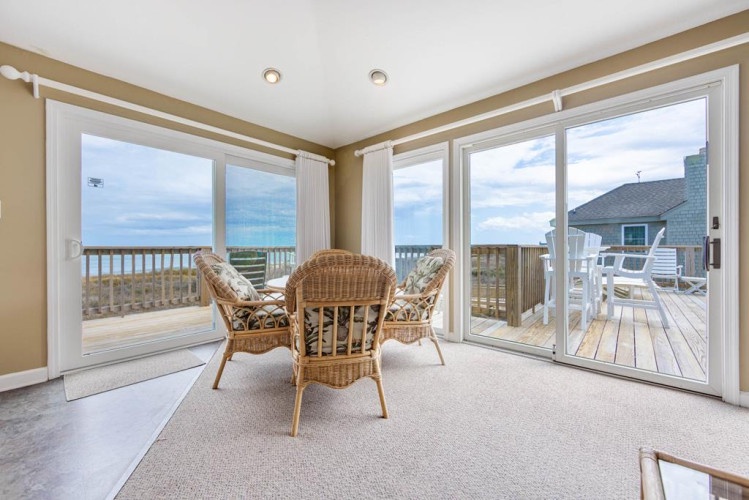Picture yourself in this bright sunroom, where wicker chairs invite you to unwind while panoramic windows frame your private view of the sea and sky beyond.