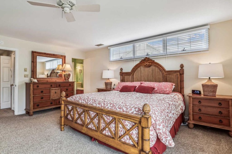 Your spacious bedroom features a handsome carved wood bed and matching furniture, ceiling fan, and soft natural light from high transom windows. Relax in your private retreat with elegant tropical touches throughout.