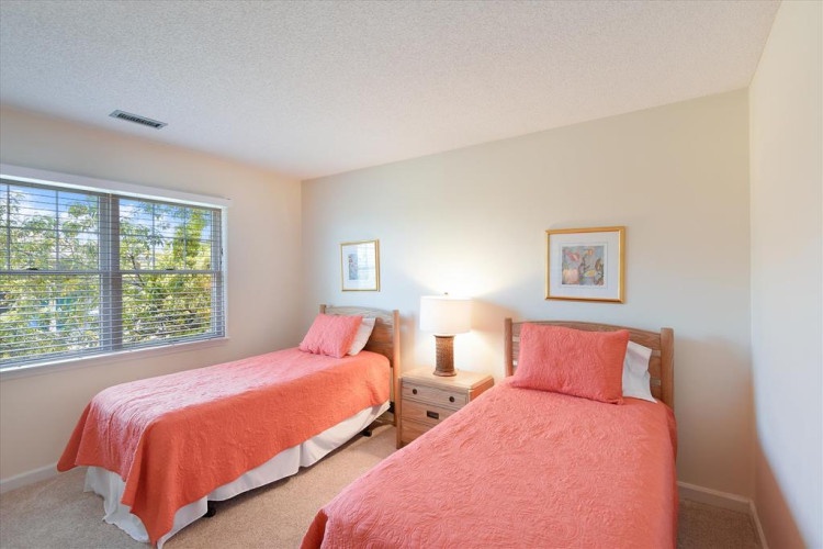 Your peaceful twin bedroom awaits, bathed in natural light and featuring cheerful coral linens. Rest easy in this cozy, thoughtfully appointed space designed for your comfort.
