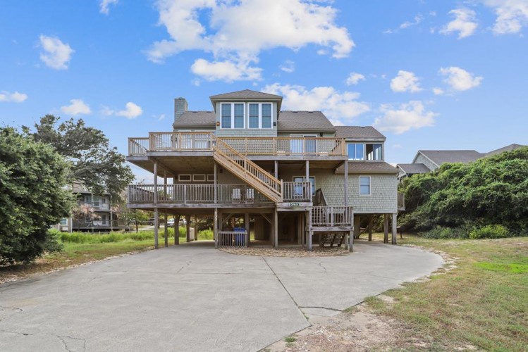 Elevated coastal beach house with spacious multi-level decks, convenient ground-level parking, and coastal vegetation in a tranquil neighborhood setting.
