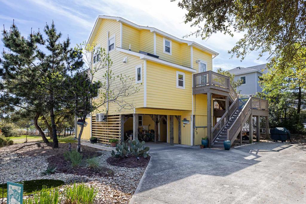 This bright yellow coastal home sits on stilts amid lush natural landscaping, offering covered parking and easy access to your beachside retreat.