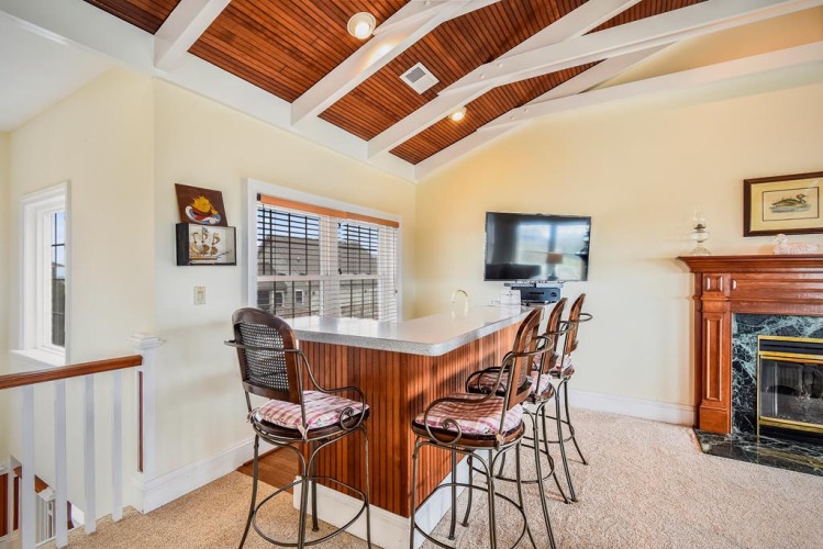 Your upstairs retreat features a cozy bar with stools perfect for morning coffee or evening cocktails, all beneath striking wood-paneled ceilings that add warmth and character.