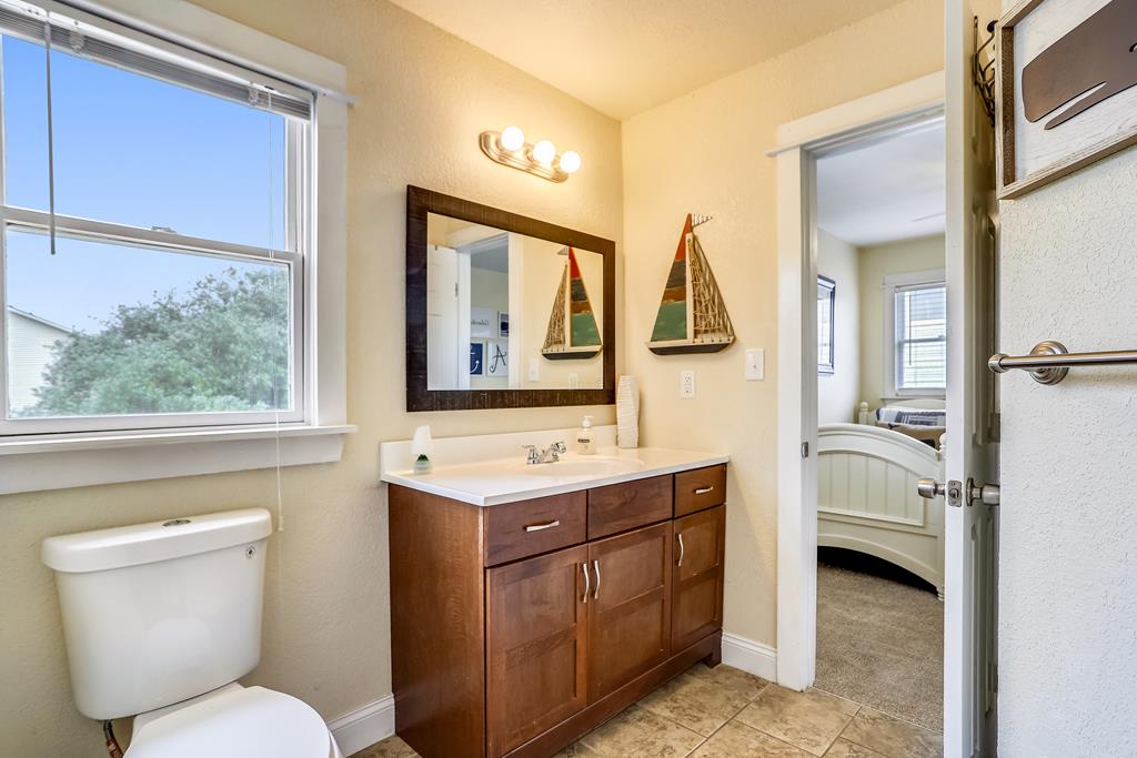 Your private bathroom features warm wood cabinetry, nautical accents, and natural light streaming through a large window, creating a bright and welcoming space to refresh.