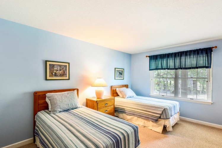 Relax in your cozy twin bedroom with soft blue walls, natural light streaming through the window, and warm wood accents creating a peaceful retreat.